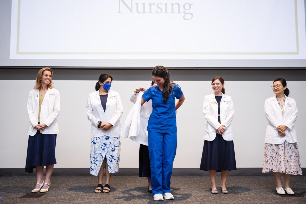 Faculty members from St. Edward's University's new nursing program look on as a student receives her white coat during the inaugural White Coat Ceremony. The historic event, held in Jones Auditorium, marks the beginning of clinical training for the university's first-ever nursing cohort. 